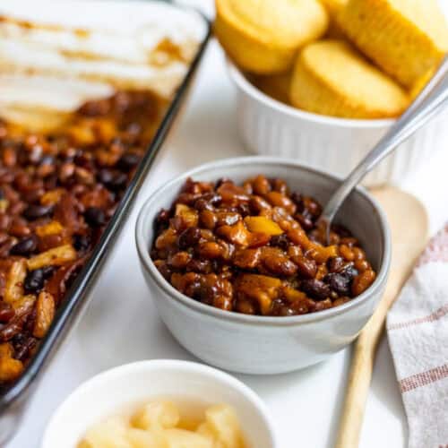 Pineapple Baked Beans in a bowl with corn bread and pan of baked beans