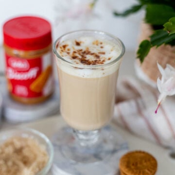A Biscoff Cookie Butter Latte with a jar of Lotus Biscoff Cookie Butter and extra Biscoff cookies.