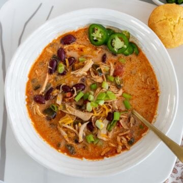 A delicious bowl of White Chicken Chili served with shredded cheddar cheese, sliced jalapenos, green onions and cornbread.