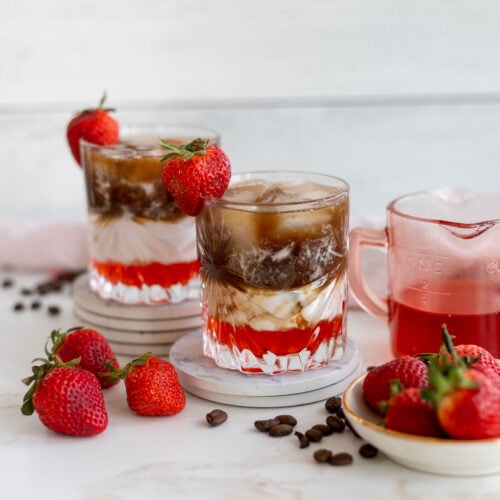 Two delicious Iced Strawberry Mocha Macchiatos with extra strawberries and coffee beans.