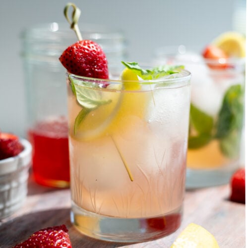 A Strawberry Basil Gin Smash garnished with strawberries, lemon wedges and basil leaves.